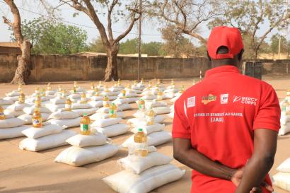 Malian mercy corps program team member stands with program supplies portioned out in the background.